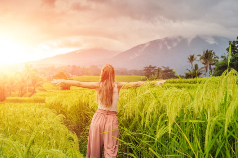 Young woman traveler on Beautiful Jatiluwih Rice Terraces against the background of famous volcanoes in Bali, Indonesia. with sunlight