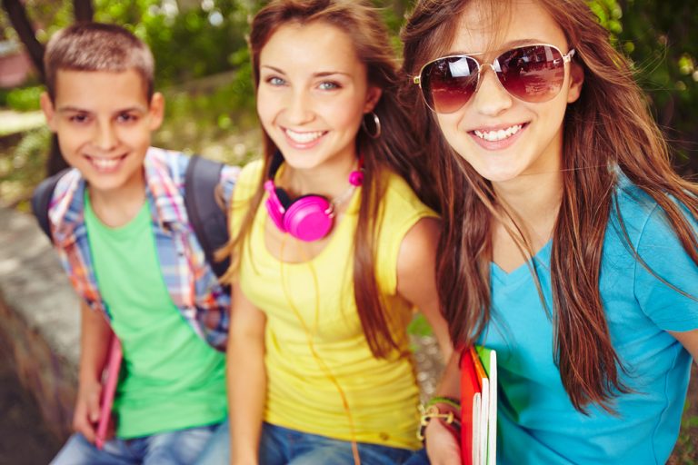 Happy teenage girls and guy looking at camera